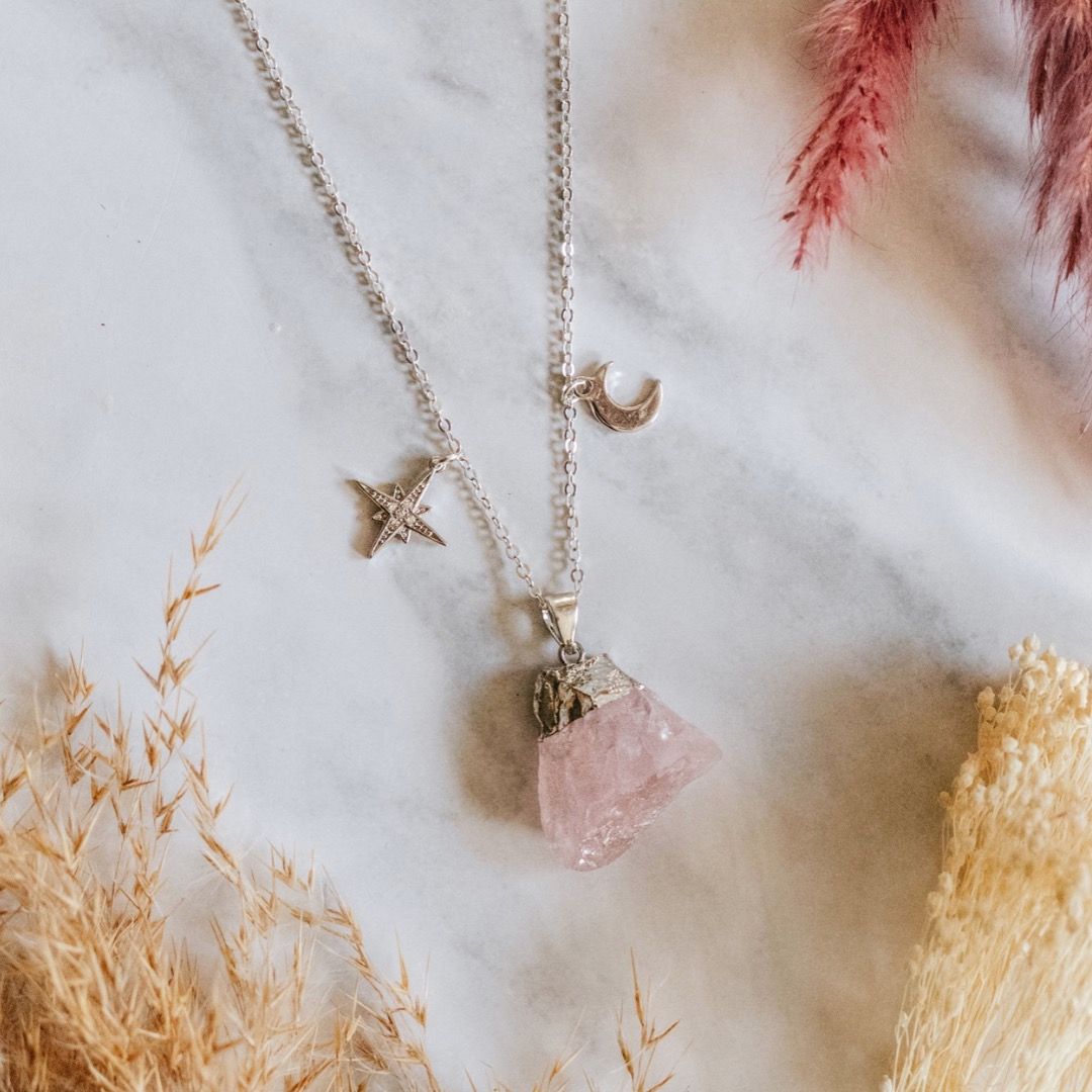 A rose quartz pendant on a necklace with a moon and star charms 