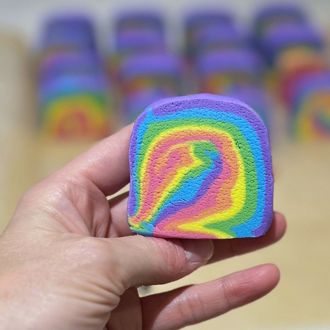 A swirling rainbow patterned bathbomb held in hand