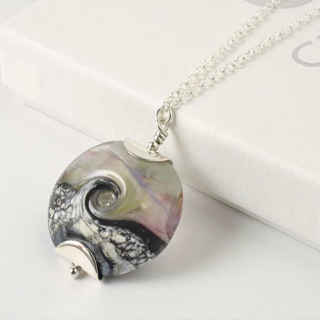A slate grey tumbled glass pendant handing from a silver hoop on a necklace