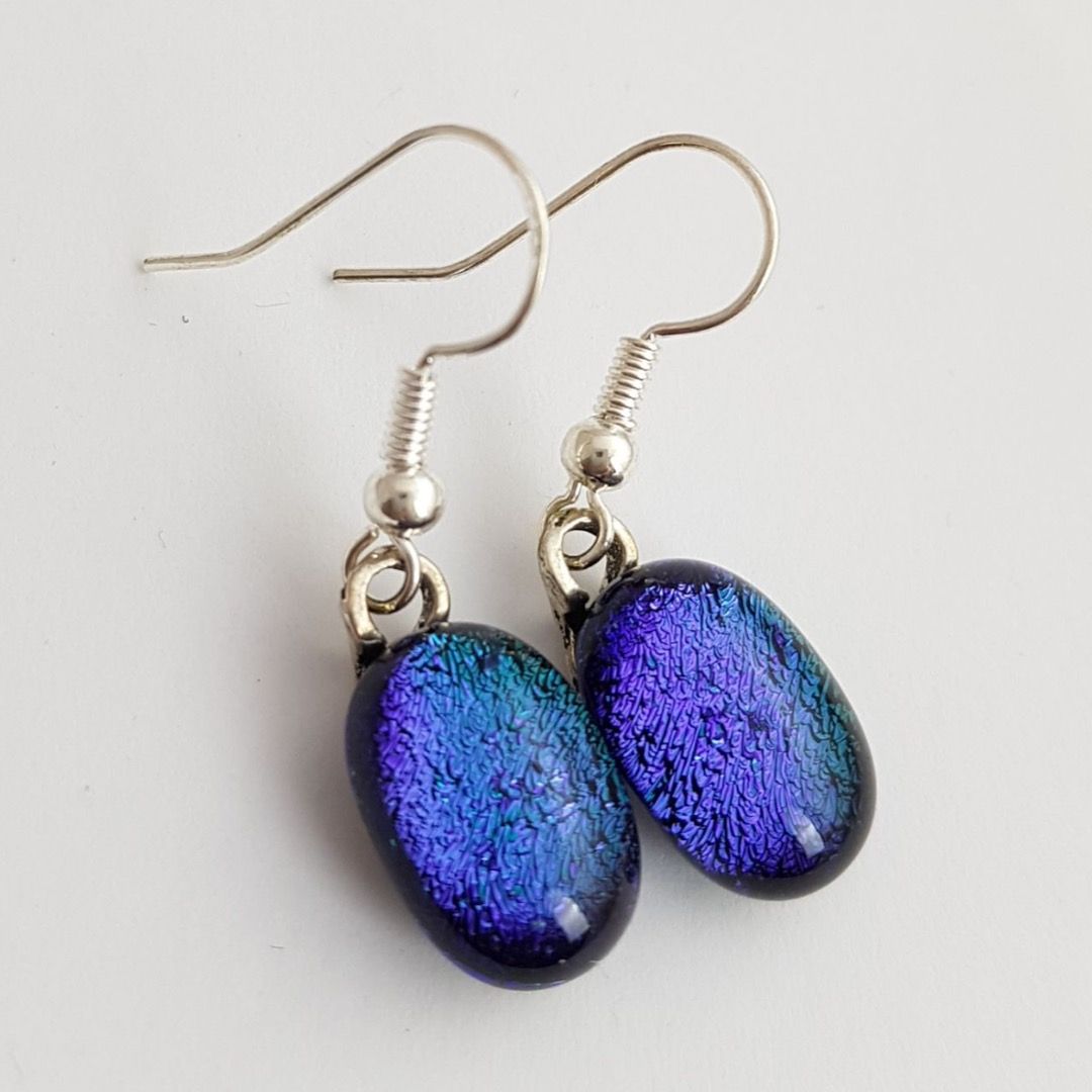 a pair of earrings featuring vibrant blues and deep purples on drop shaped charms in a dichroic effect
