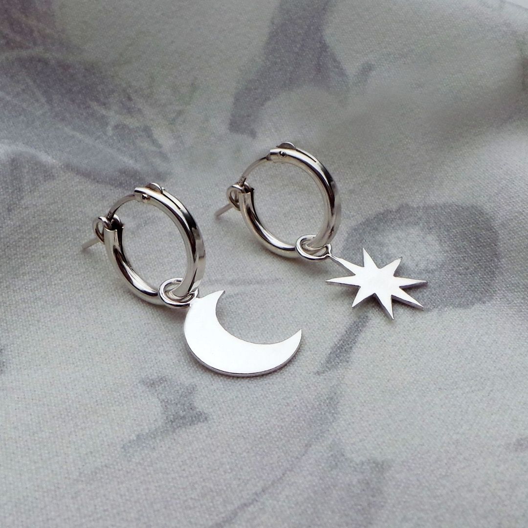 a pair of sterling silver hoop earrings, one with a moon charm and the other a star
