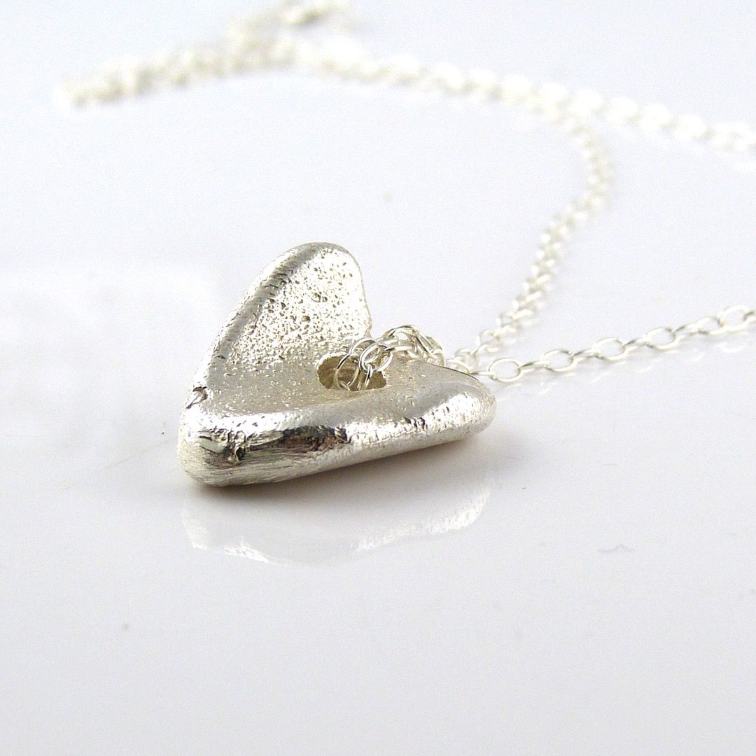A sterling silver heart charm with a light dappled effect on a dainty necklace
