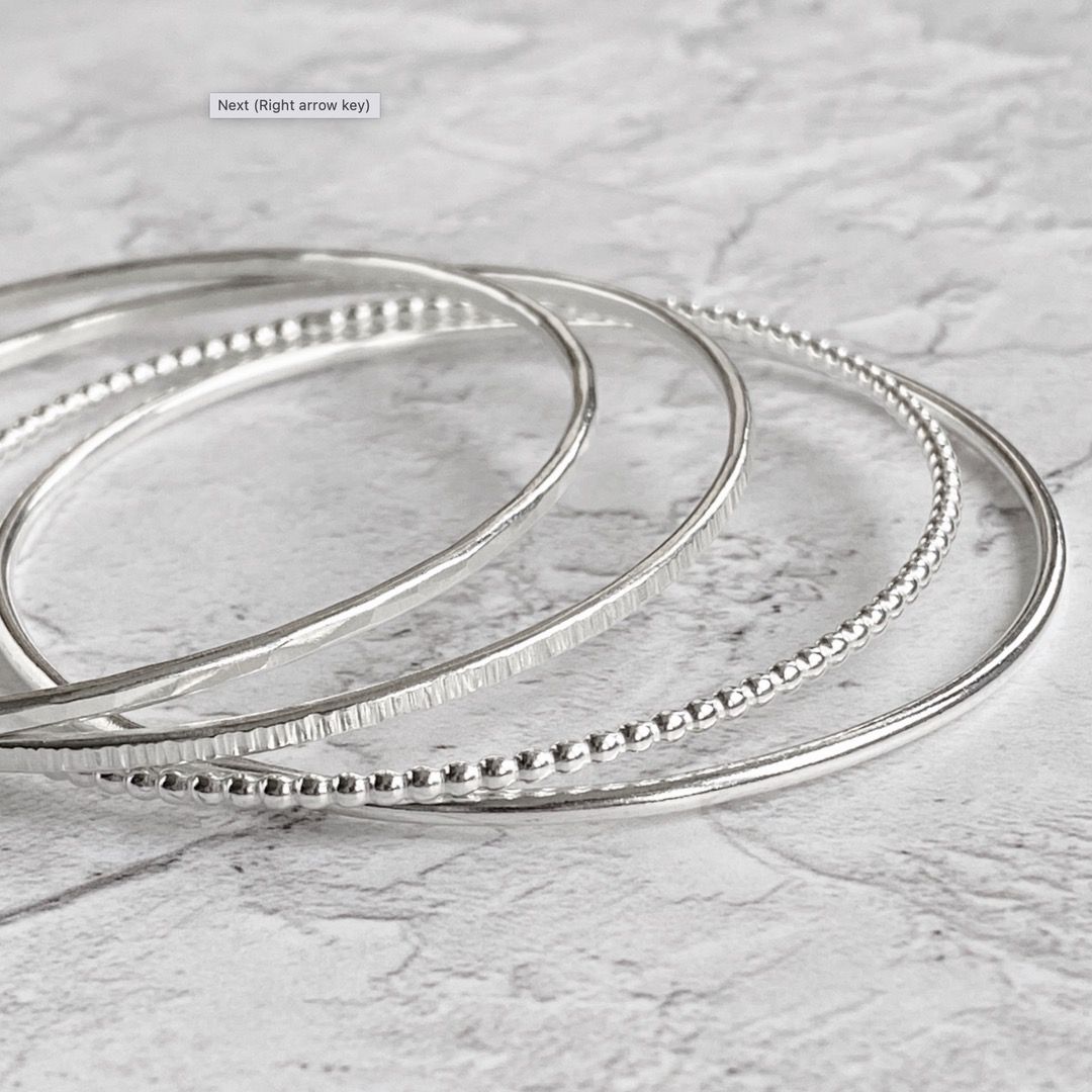 Four sterling silver bangles with different styles and textures on a marble surface