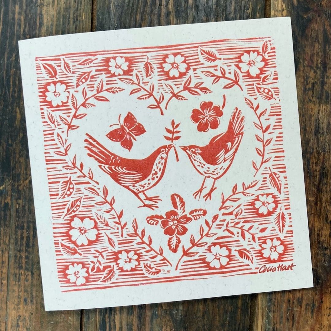 A red stencil print card with two mistle thrushes in the shape of a foliage heart