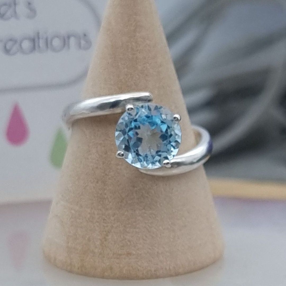A silver ring that swirls each side of a large sky blue topaz