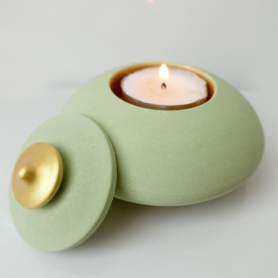 A green, oval candle holder with its lid resting to the side