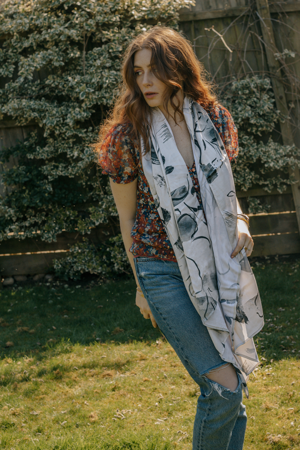 A person wearing a long white scarf with an abstract flower pattern