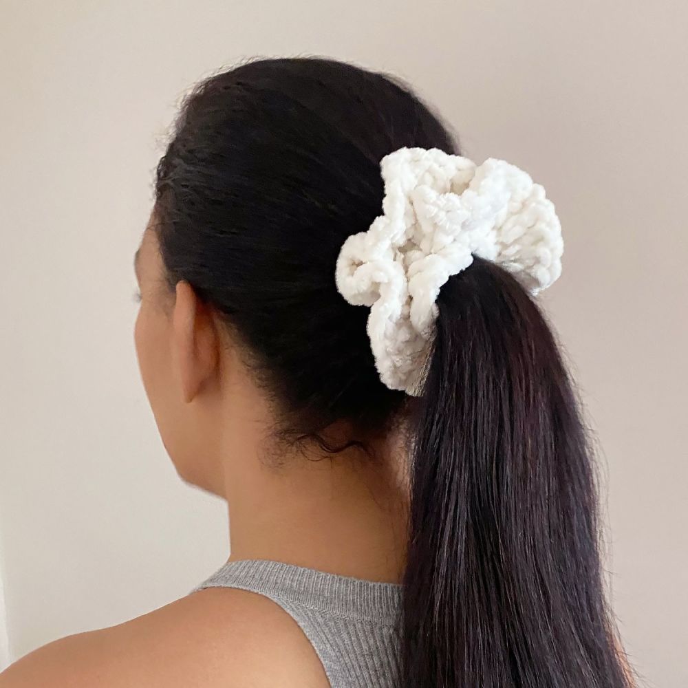 A person with long black hair wearing a soft cream velvet crochet scrunchie