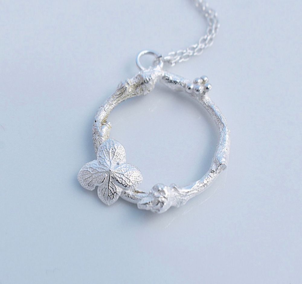 A silver woodland wreath necklace featuring leaves and berries