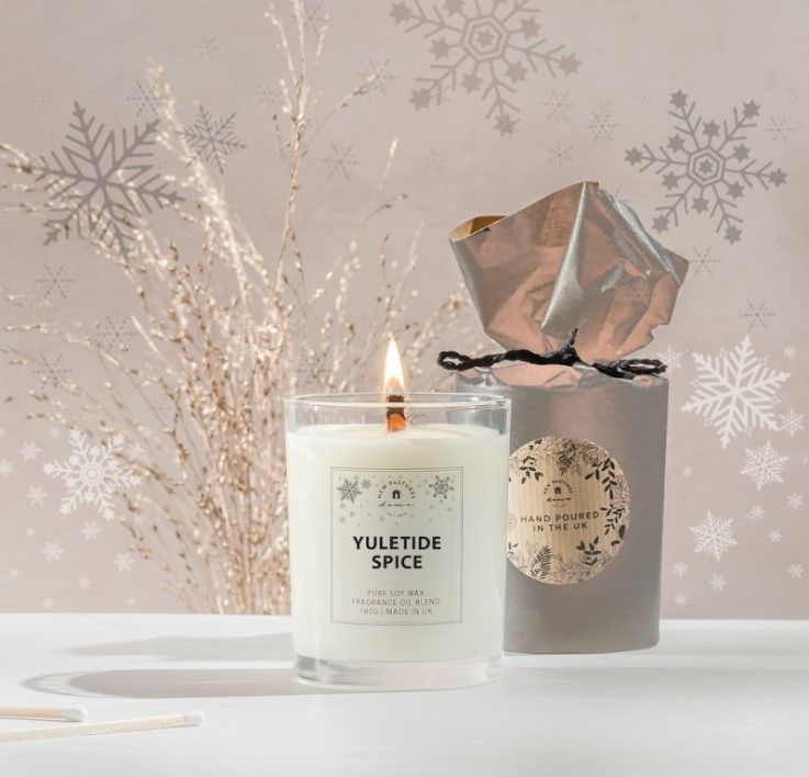 A white Yuletide Spice glowing candle against a festive backdrop