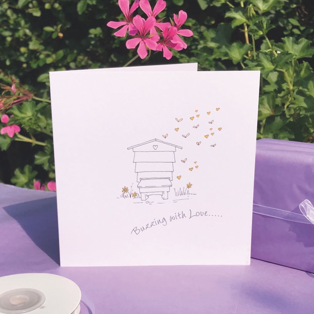 A card featuring a drawn beehouse with bees and hearts flying from it.