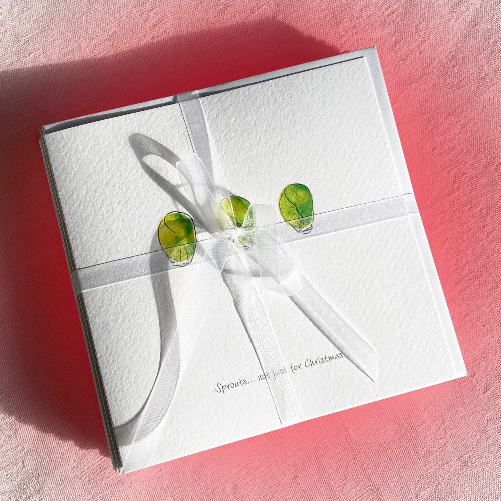 A bundle of christmas cards wrapped in a white ribbon. The top card features 3 sprouts
