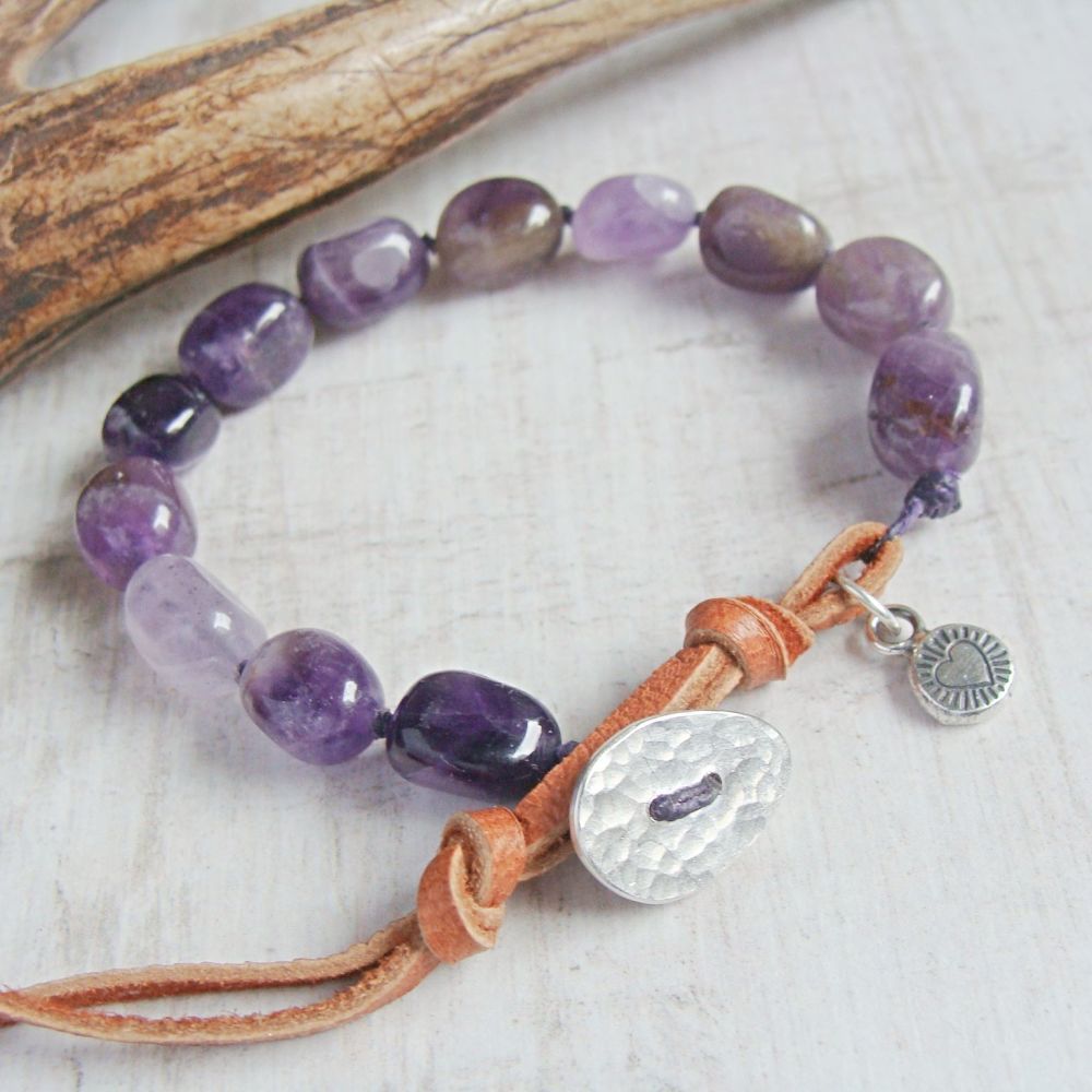 A bracelet of amethyst pebbles and silver charms with a deer skin clasp