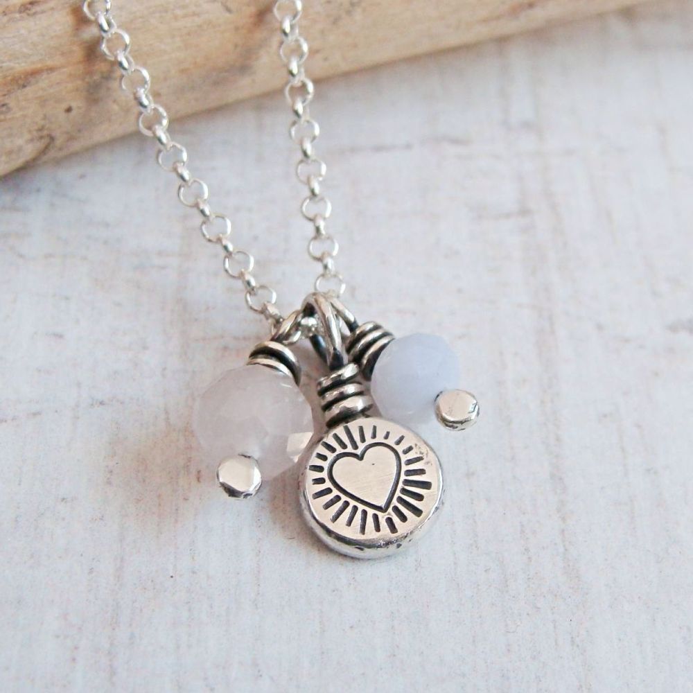 A silver charm necklace featuring two pale gems and a stamped heart design