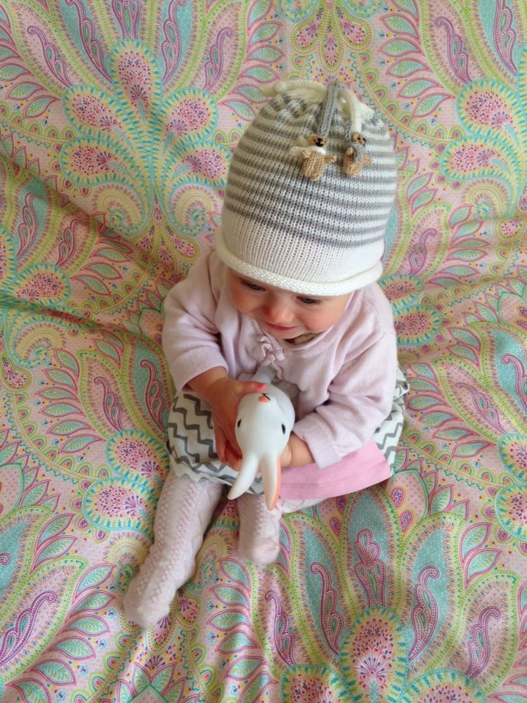 A baby wearing a two striped white and grey teddy hat