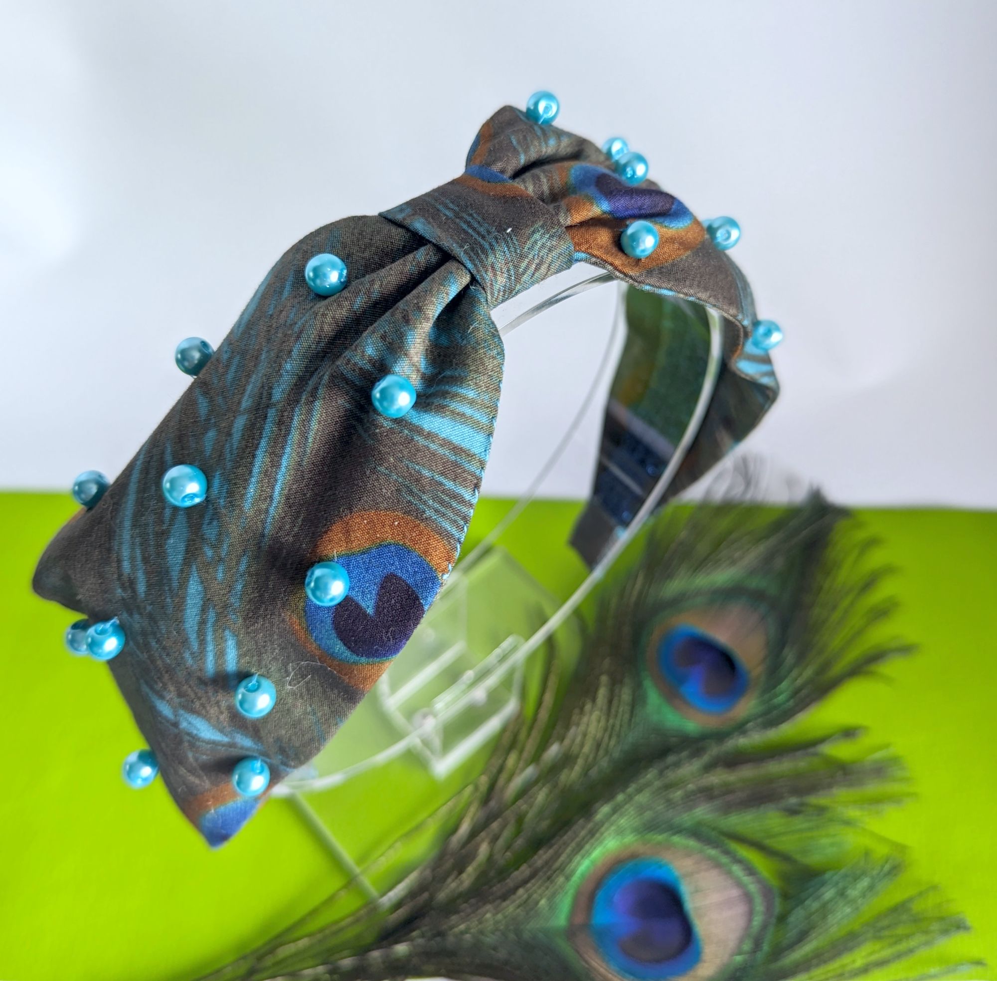 a headband with a peacock feather print, adorned with blue beads