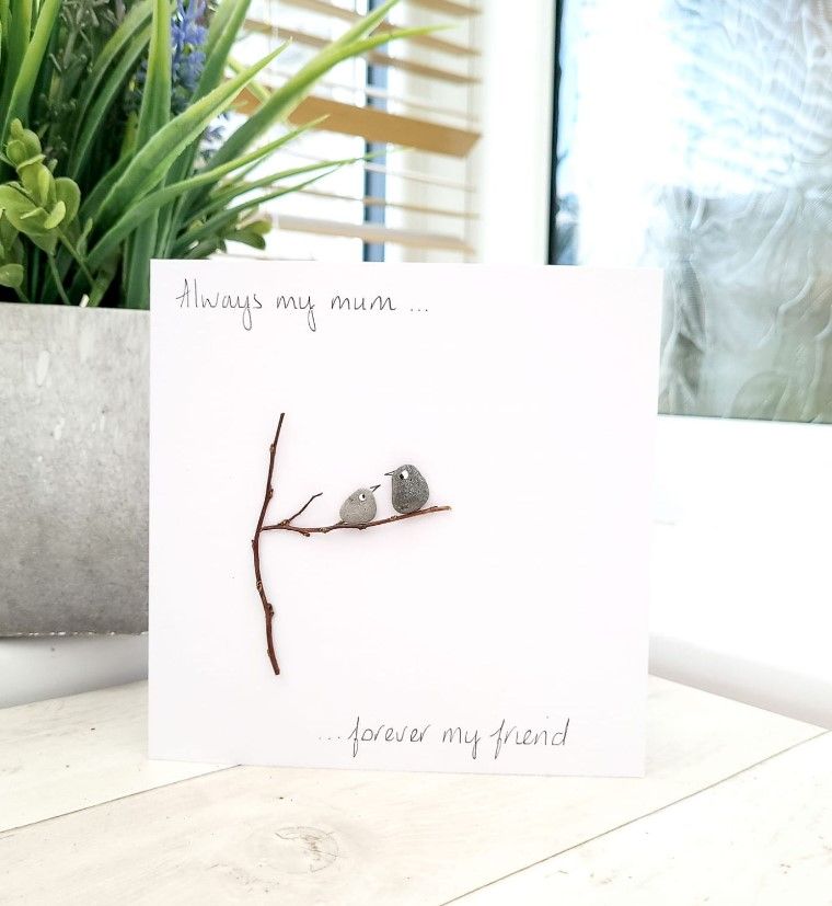 A card featuring pebble art of two birds perched on a branch