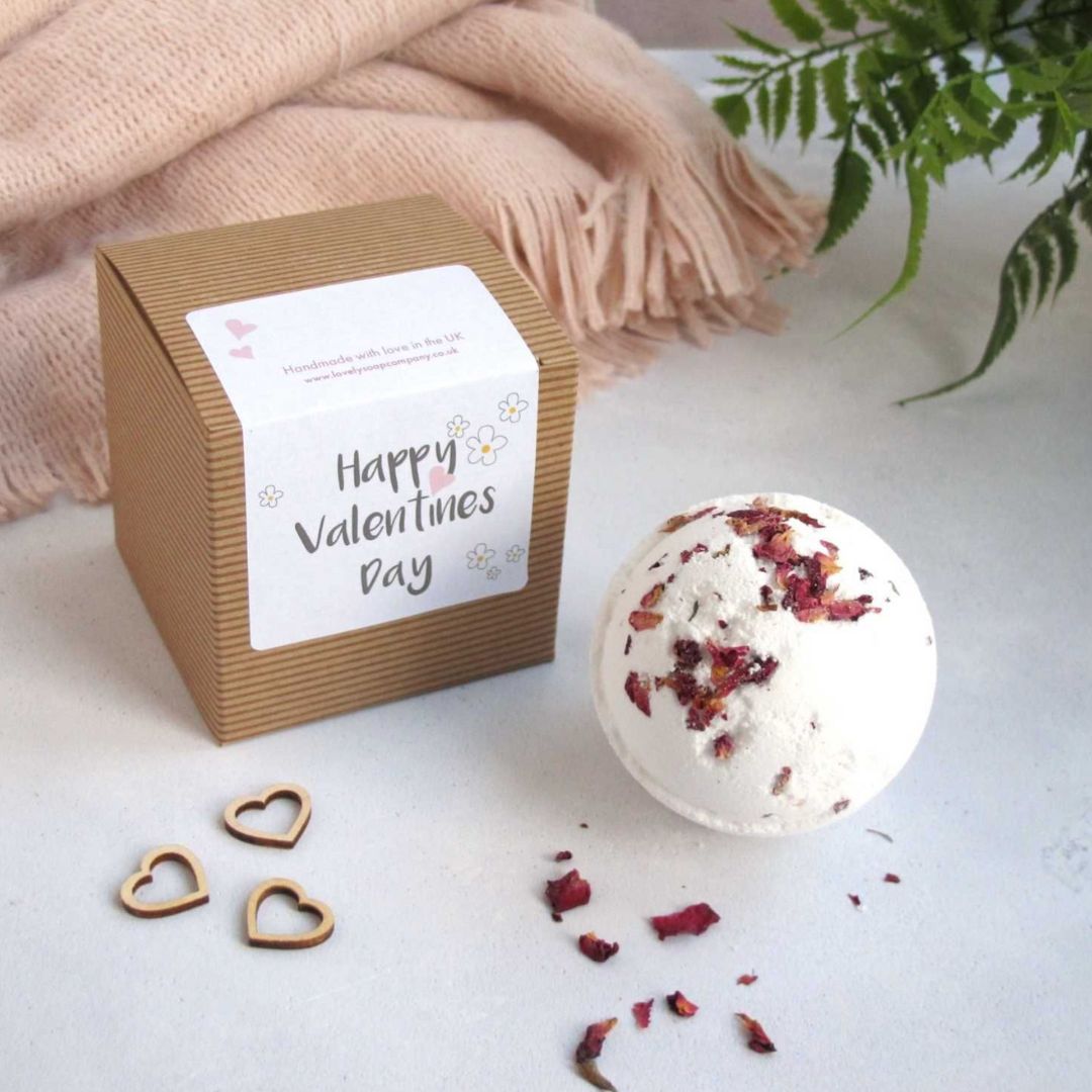 A white bath bomb with rose petals featured next to its gift box
