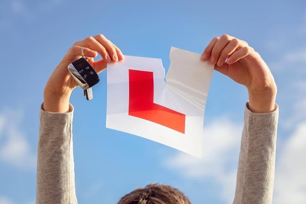 Hands holding ripped L plate and car keys against blue sky