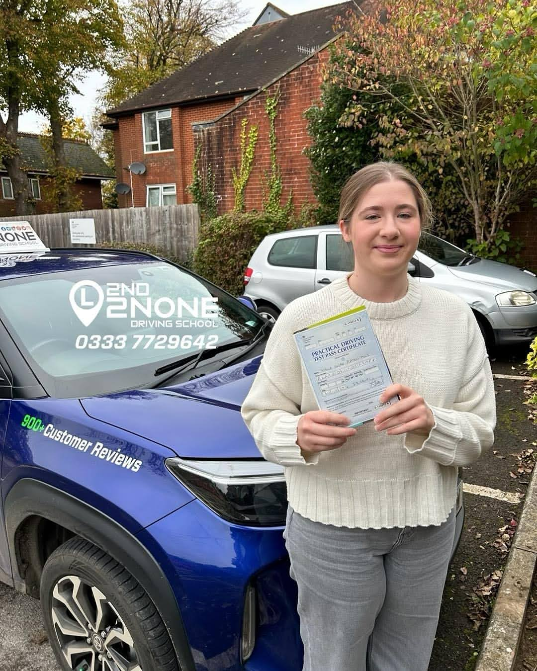 Student holding driving test pass certificate beside driving school car