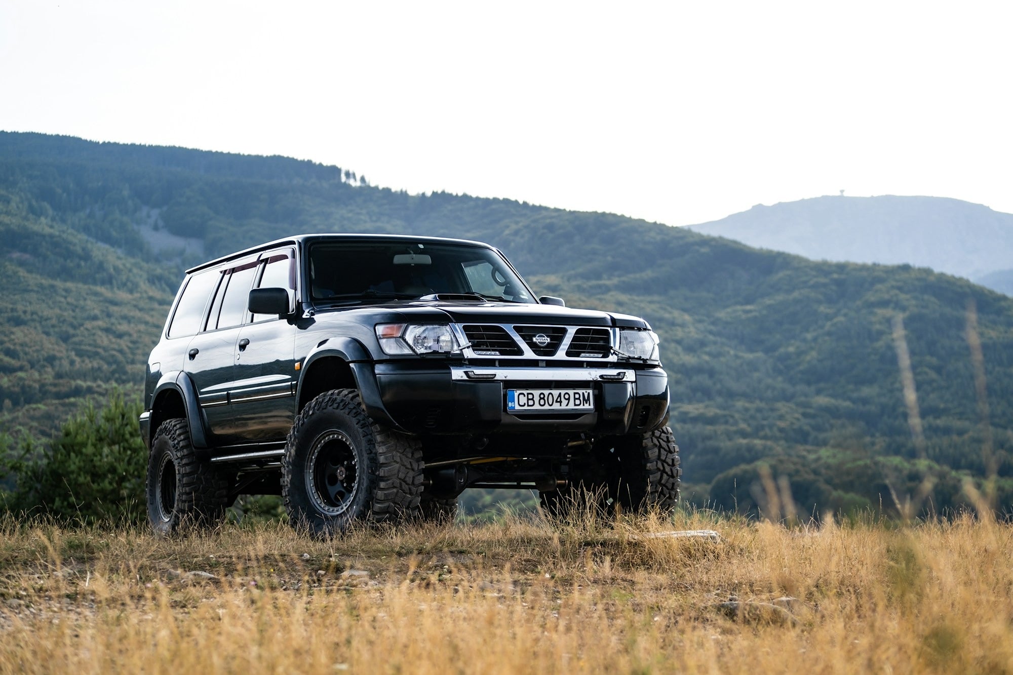 a-black-suv-parked-in-a-field-with-mountains-in-the-background-Gjhd1ou3VhU