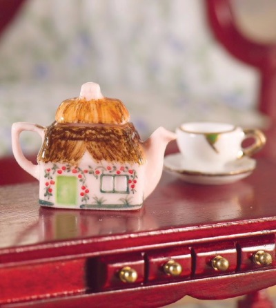 A dollshouse miniature cottage teapot and teacup on a 12th scale mahogany sideboard