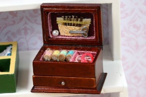 An open miniature sewing box, filled with dollhouse sized accessories for sewing