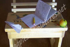 A model school desk with an open notebook with writing and a paper airplane