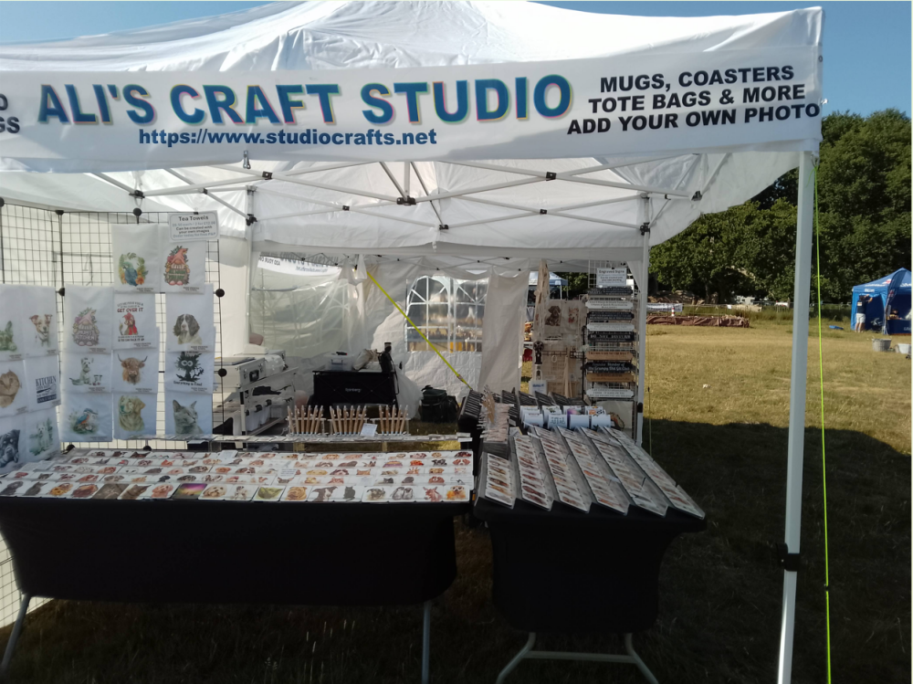 A large white gazebo with Alis Craft Studio banner and array of products for sale