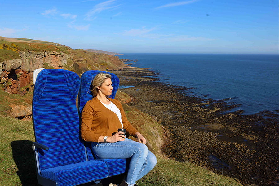 Promotional image from Lumo showing a person sat in a Lumo seat in a seaside setting