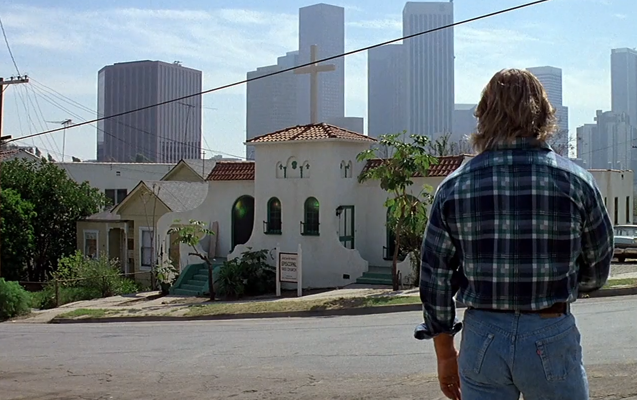 John Nada pauses in front of a church while navigating the hidden alien-controlled world in They Live
