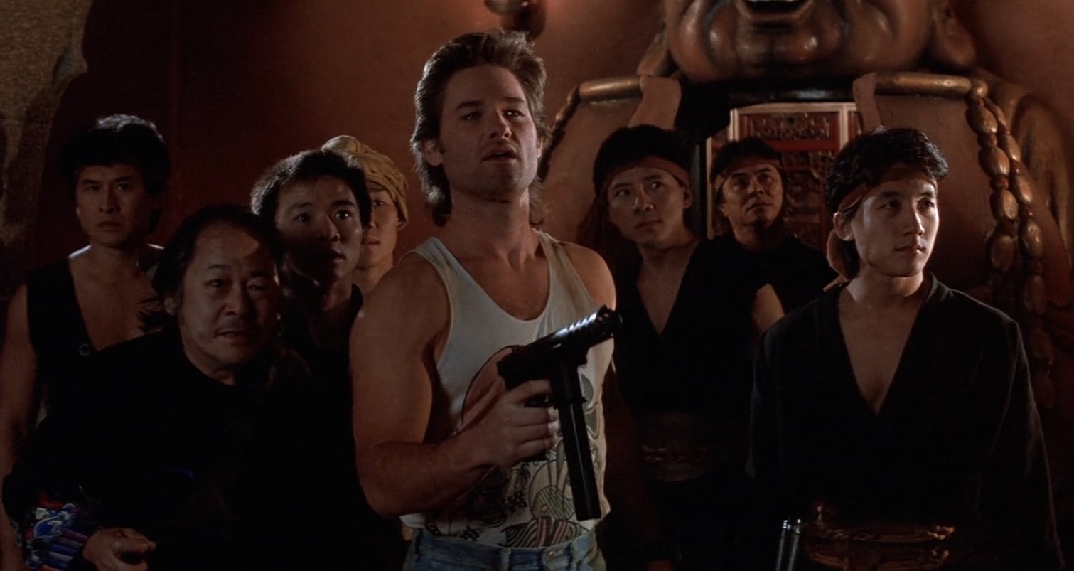 Image shows Jack Burton and his allies cautiously entering a dimly lit underground chamber, where a mysterious wedding ceremony is taking place