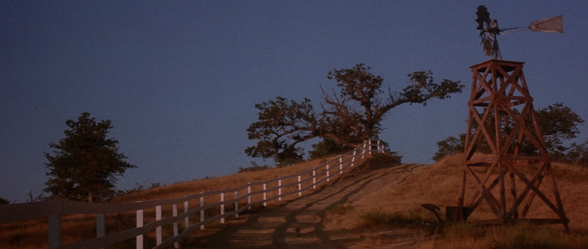 Opening scene of Critters showing a rural landscape with a trail, fence, and tower
