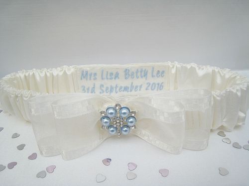 An ivory wedding garter which has blue pearls stitched on the front, blue wedding details on the inside.