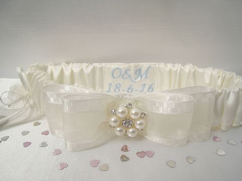 Photo of a wedding garter made from ivory satin and embroidered with blue initials and a wedding date.