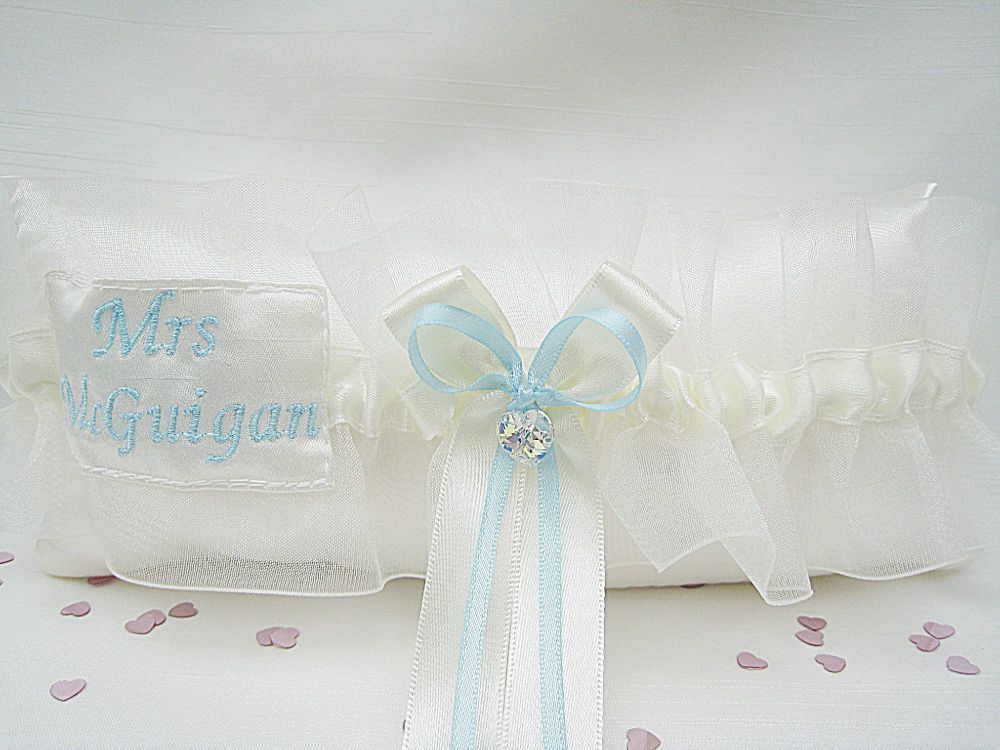 Picture of a wedding garter with a Swarovski Crystal in the centre and a pocket to the side which holds a silver sixpence.