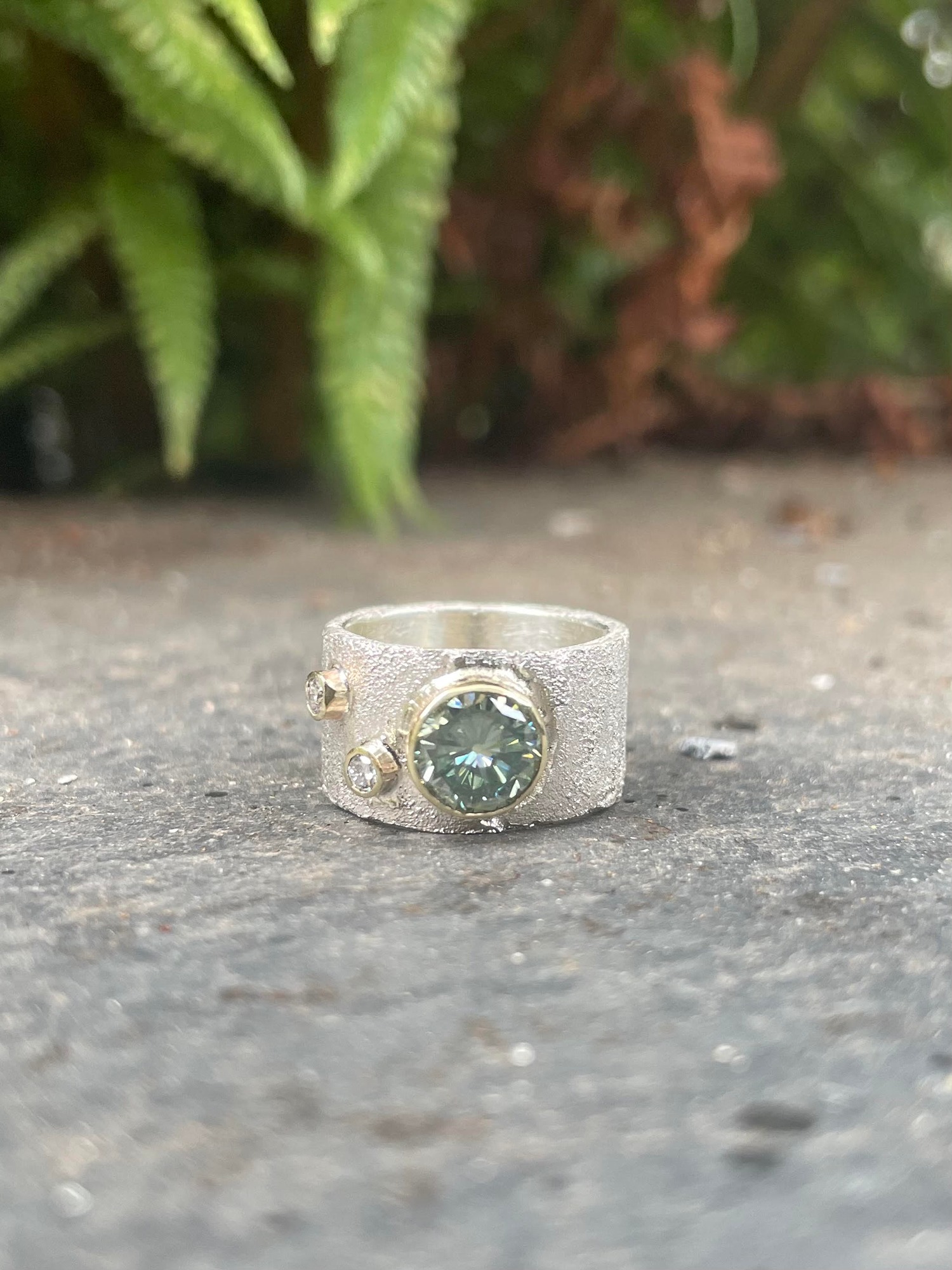 Rivda collection flat silver band with a glistening frozen sand texture and a gemstone set in a signature gold rubover setting.
