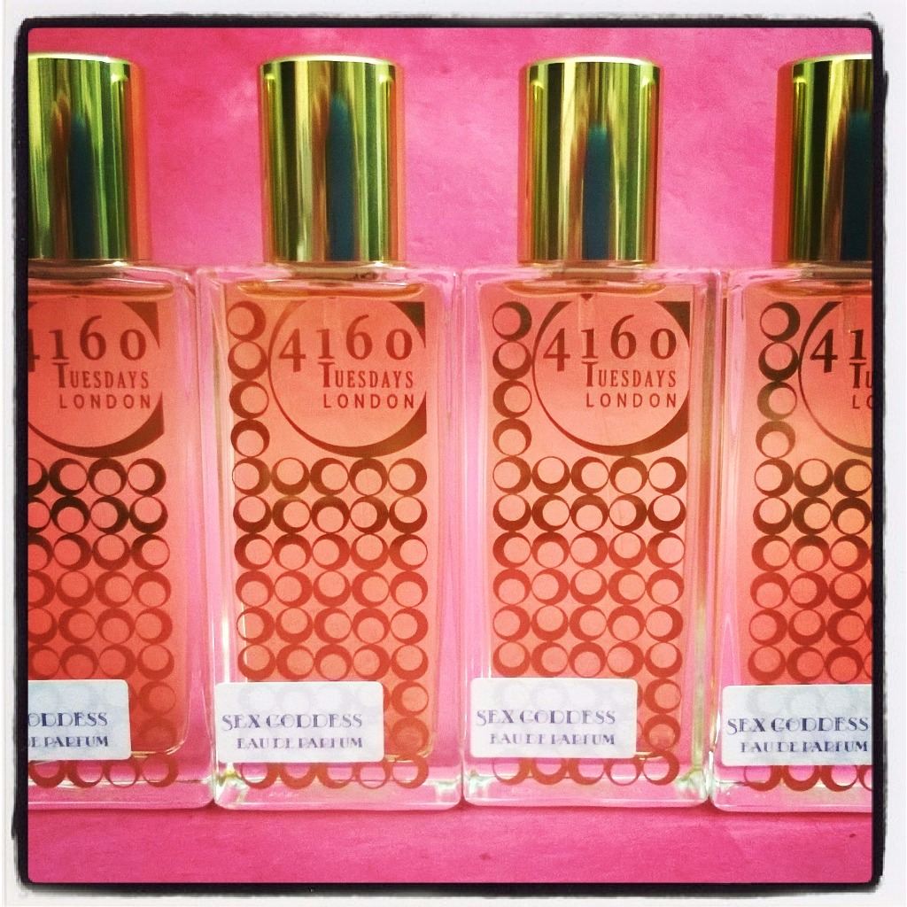 Four gold bottles of 4160Tuesdays perfume against a pink background.