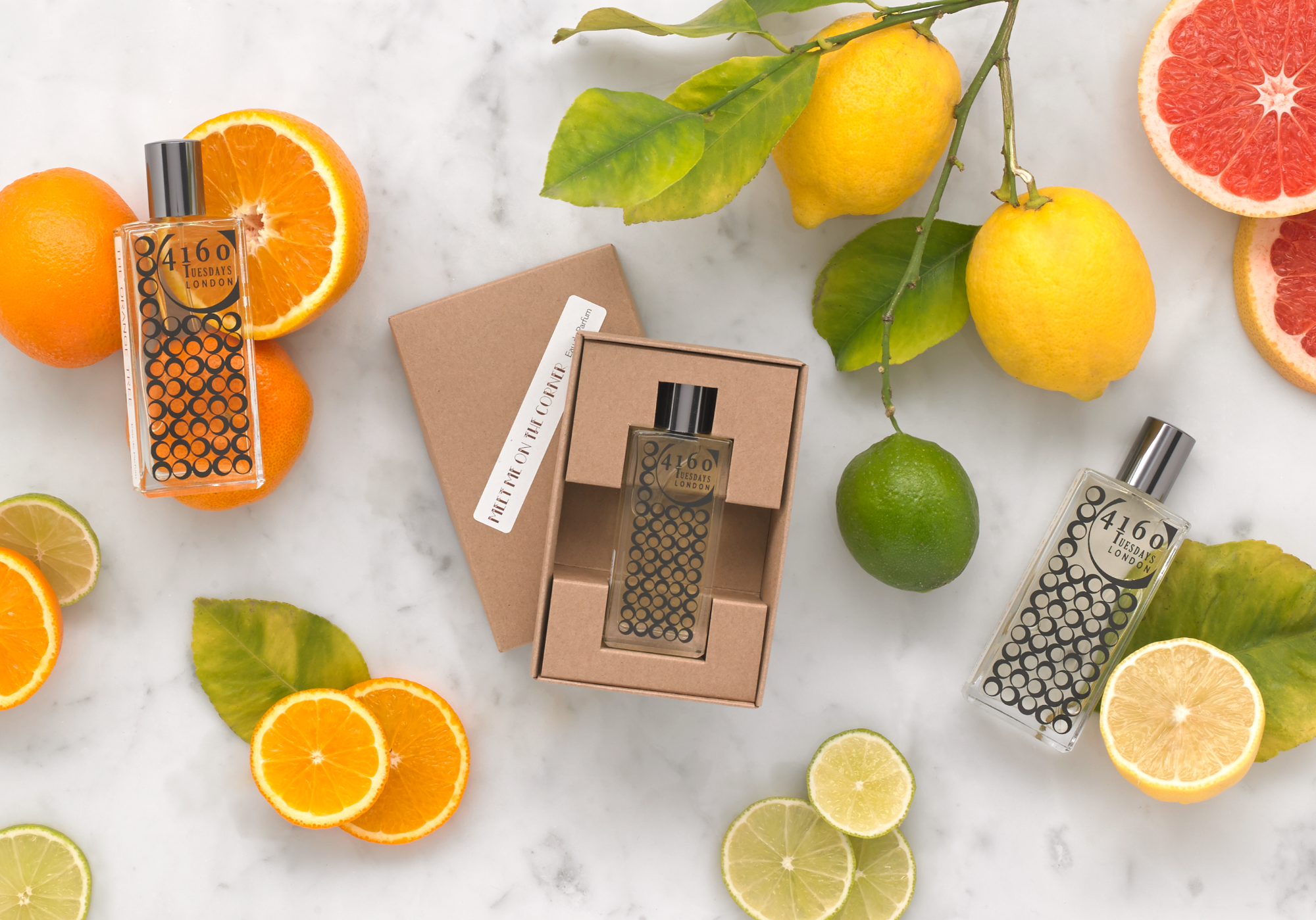 Stylised photo of a bottle of 4160 Tuesdays perfume surrounded by oranges, lemons and limes