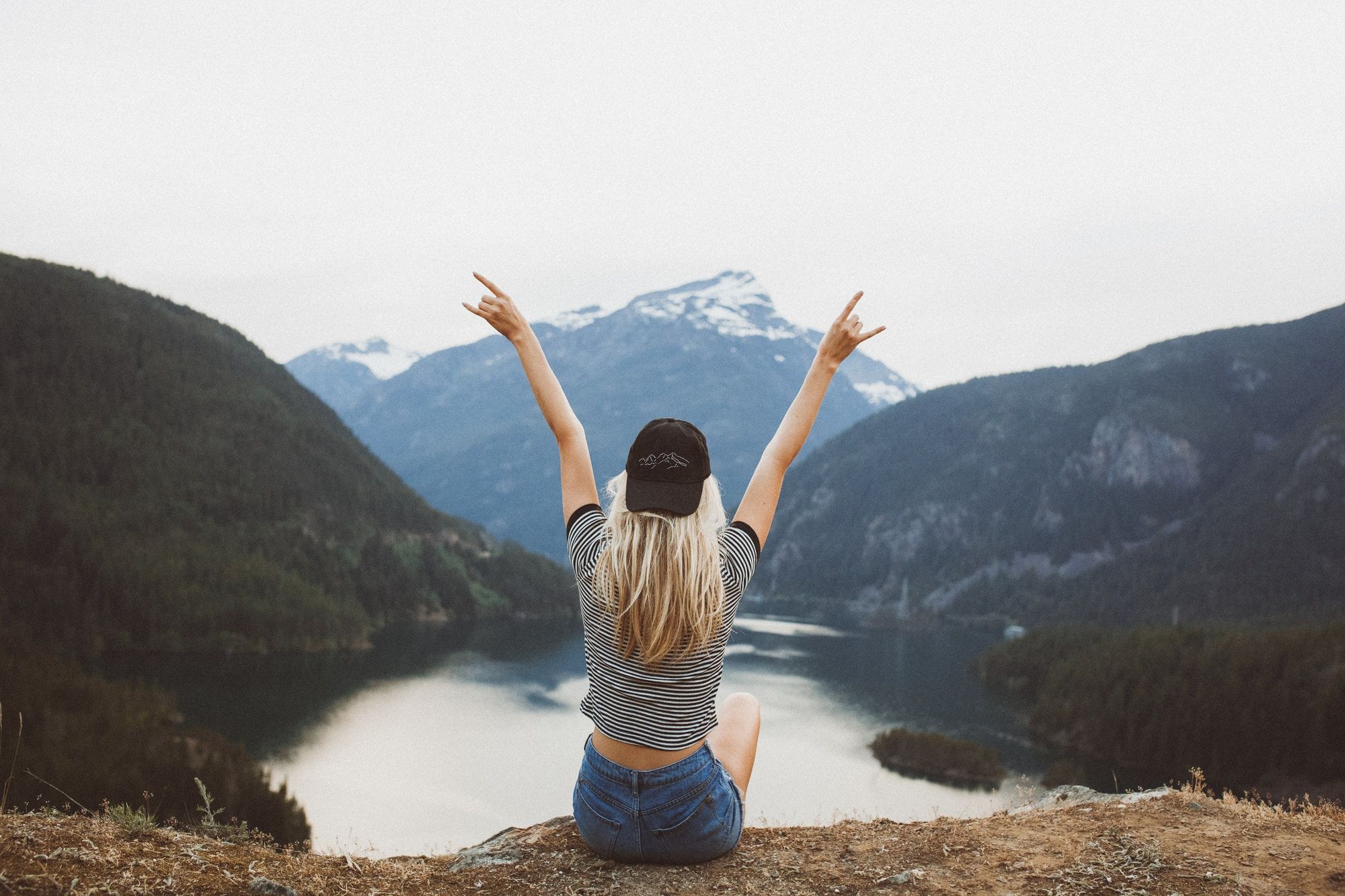 Woman sat on mountain edge with both arms raised