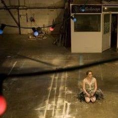 A woman in ballerina outfit sits on the floor of an industrial space 