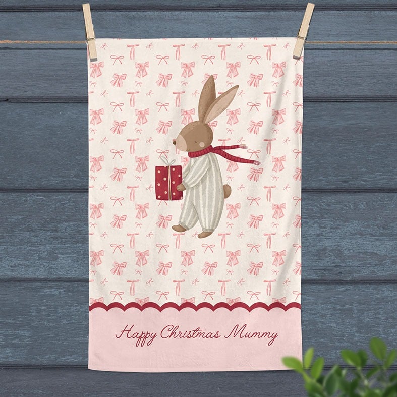 Personalised cotton Christmas tea towel with hand-drawn festive bunny illustration on a background of pink bows