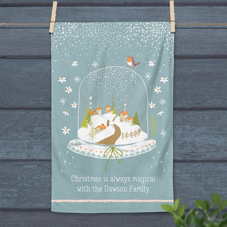 Personalised cotton Christmas tea towel in pale blue with snowy hand-drawn snowglobe village illustration