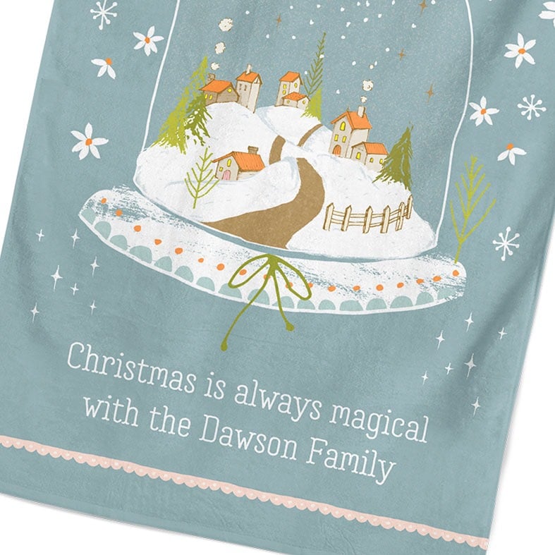 Personalised cotton Christmas tea towel in pale blue with snowy hand-drawn snowglobe village illustration