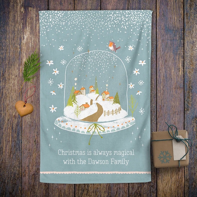 Personalised cotton Christmas tea towel in pale blue with snowy hand-drawn snowglobe village illustration