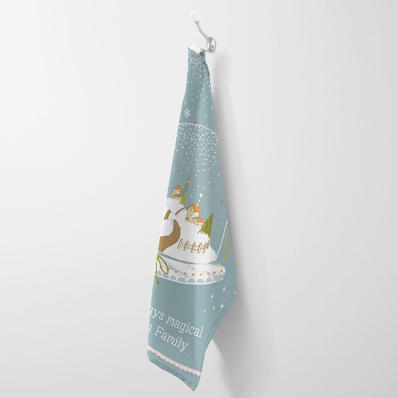 Personalised cotton Christmas tea towel in pale blue with snowy hand-drawn snowglobe village illustration