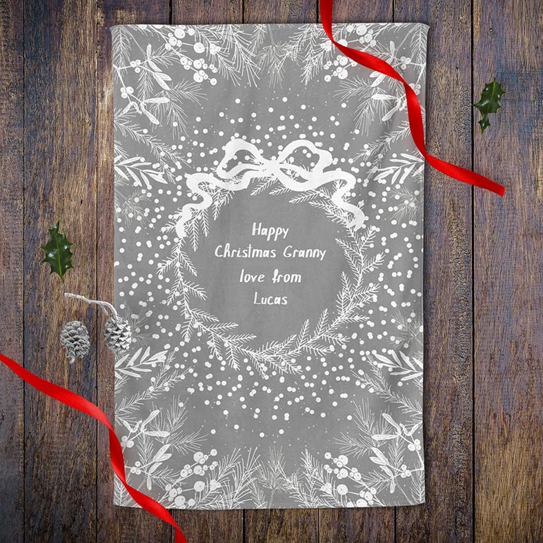 Personalised cotton Christmas tea towel in pale grey and white with white winter wreath, leaves, and berries