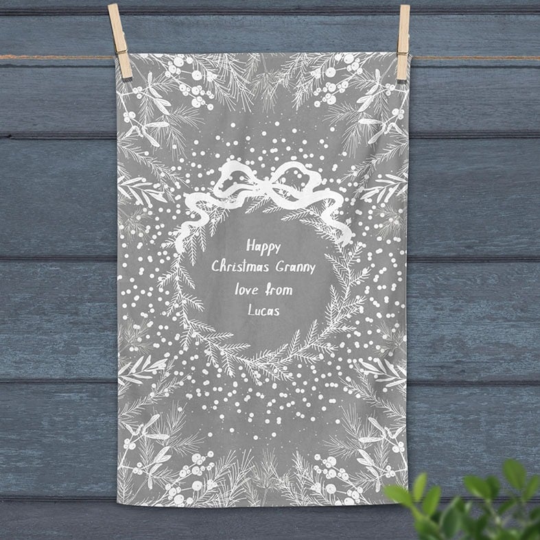 Personalised cotton Christmas tea towel in pale grey and white with white winter wreath, leaves, and berries