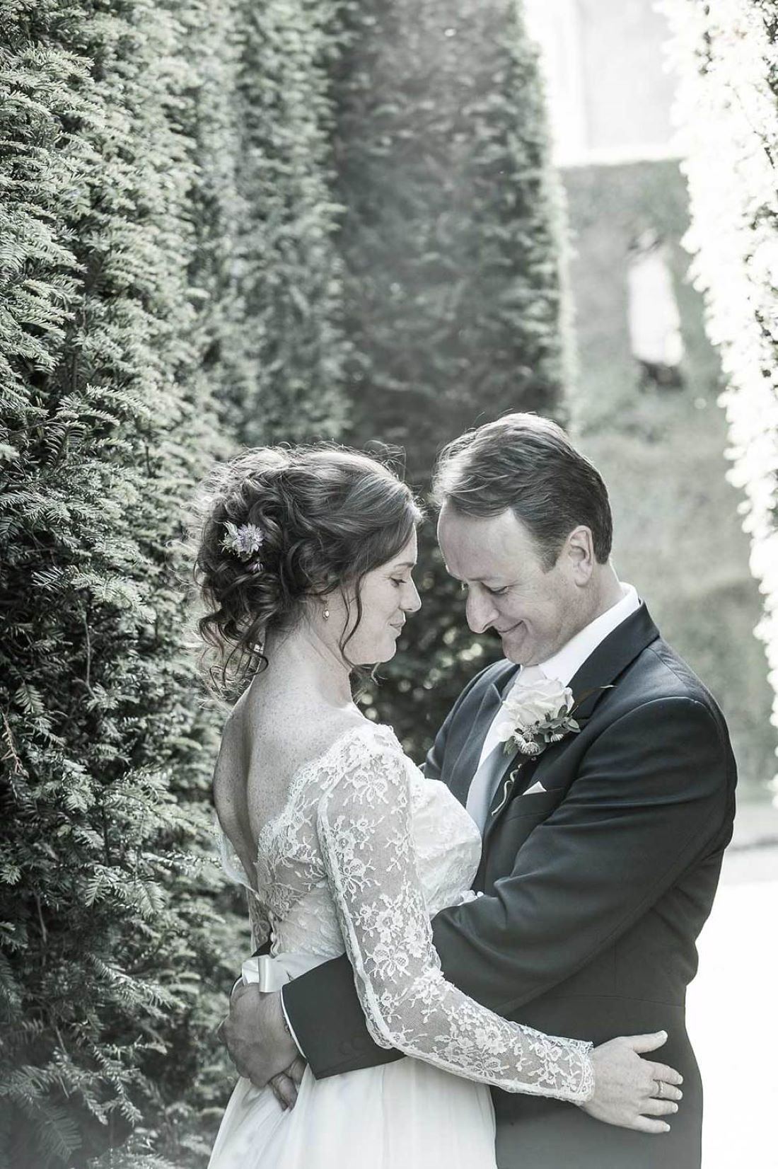 bride wearing a lace bridal dress with her hair styled in a messy bun facing her groom-bridal hair styled-in natural curls