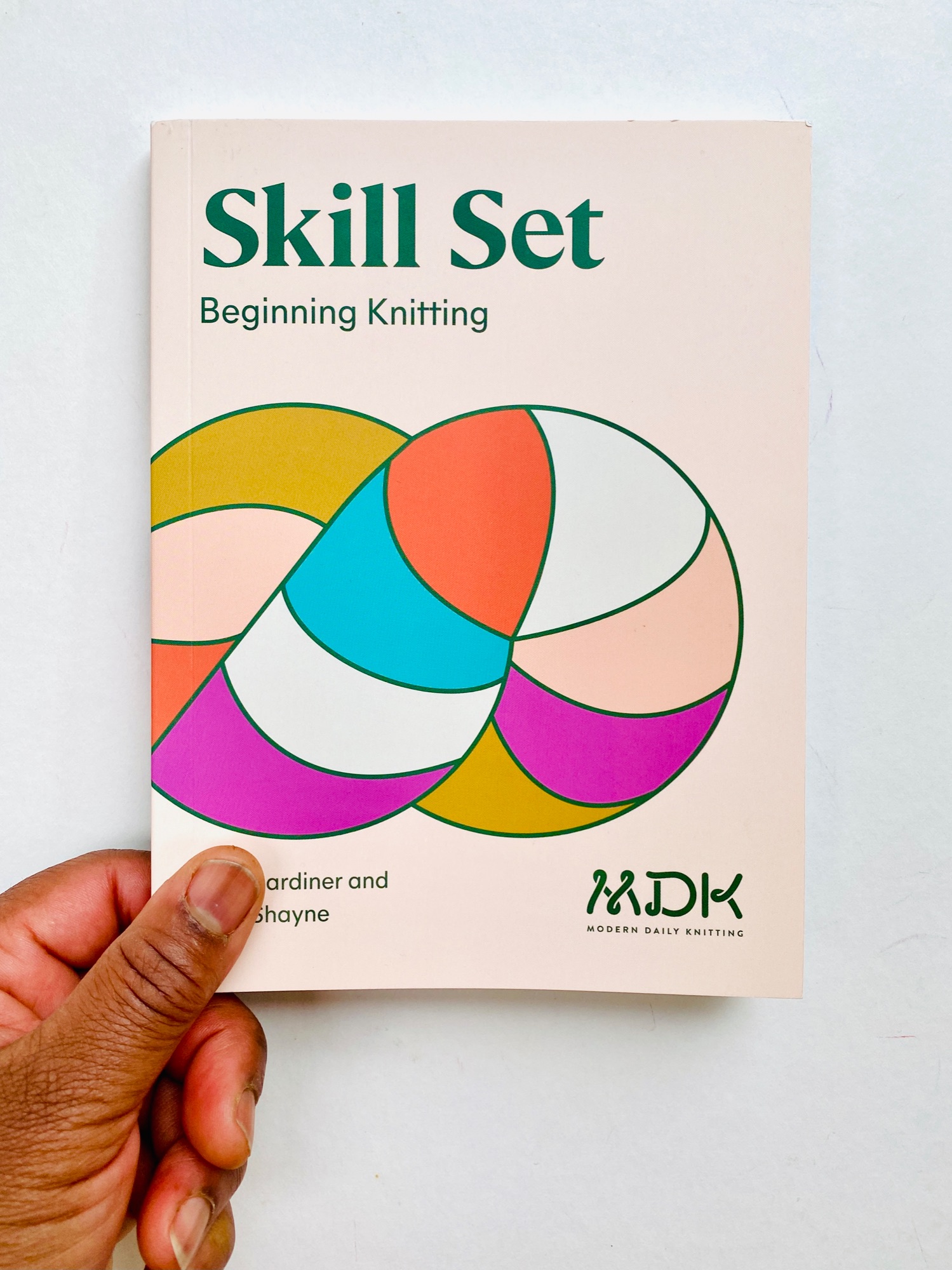 image of a black woman's left hand holding a print copy of Shill Set Beginner `Knitting by Modern Daily Knitting